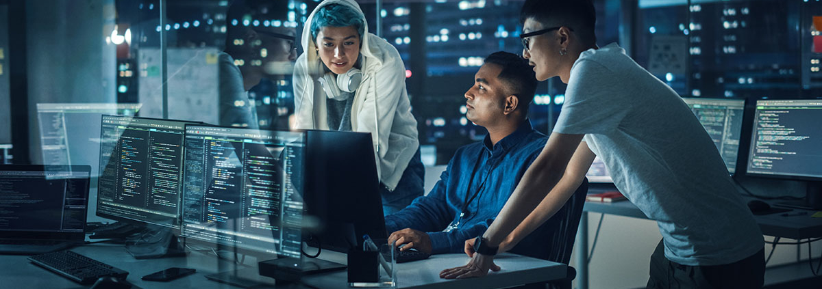 Diverse Team of Professionals Meeting in Office at Night: Brainstorming IT Programmers Use Computer Together, Talk Strategy, Discuss Planning. Software Engineers Develop Inspirational App Program