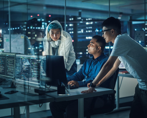 Diverse Team of Professionals Meeting in Office at Night: Brainstorming IT Programmers Use Computer Together, Talk Strategy, Discuss Planning. Software Engineers Develop Inspirational App Program