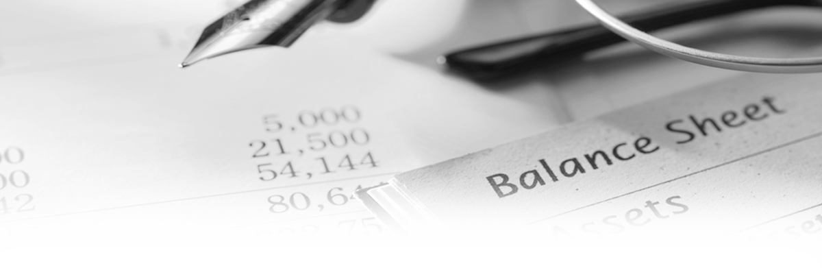 Photograph of balance sheets with a fountain pen and glasses laying on top of them.